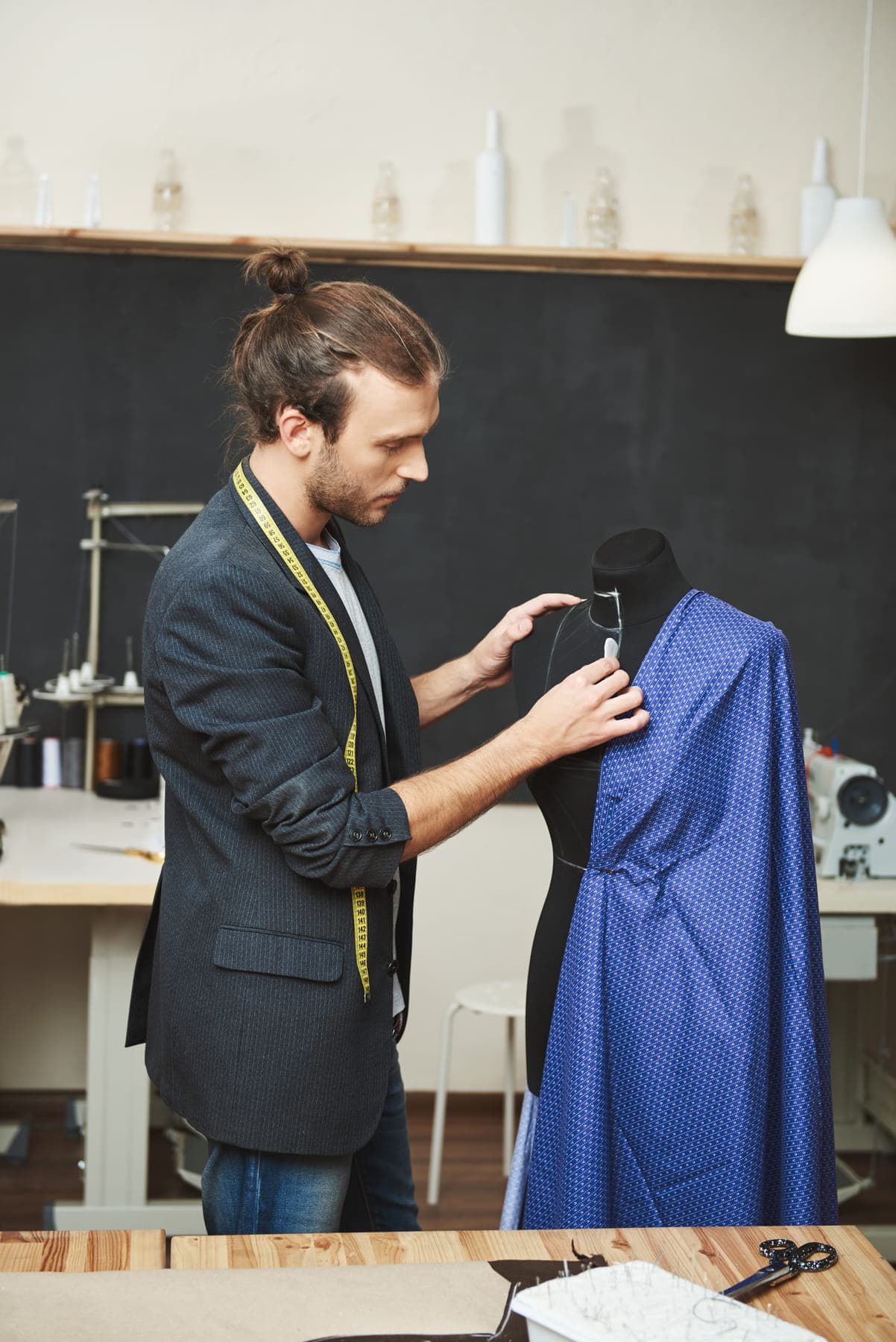 A tailor pinning patterned fabric to a dress form in a workroom.